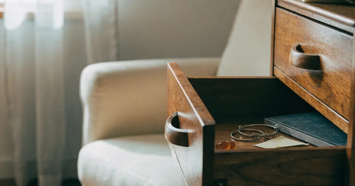 Il cassetto aperto di un cassettone di legno accanto a una poltrona, con alcuni gioielli e una scatola all'interno, che evoca il disordine dopo un furto in casa.